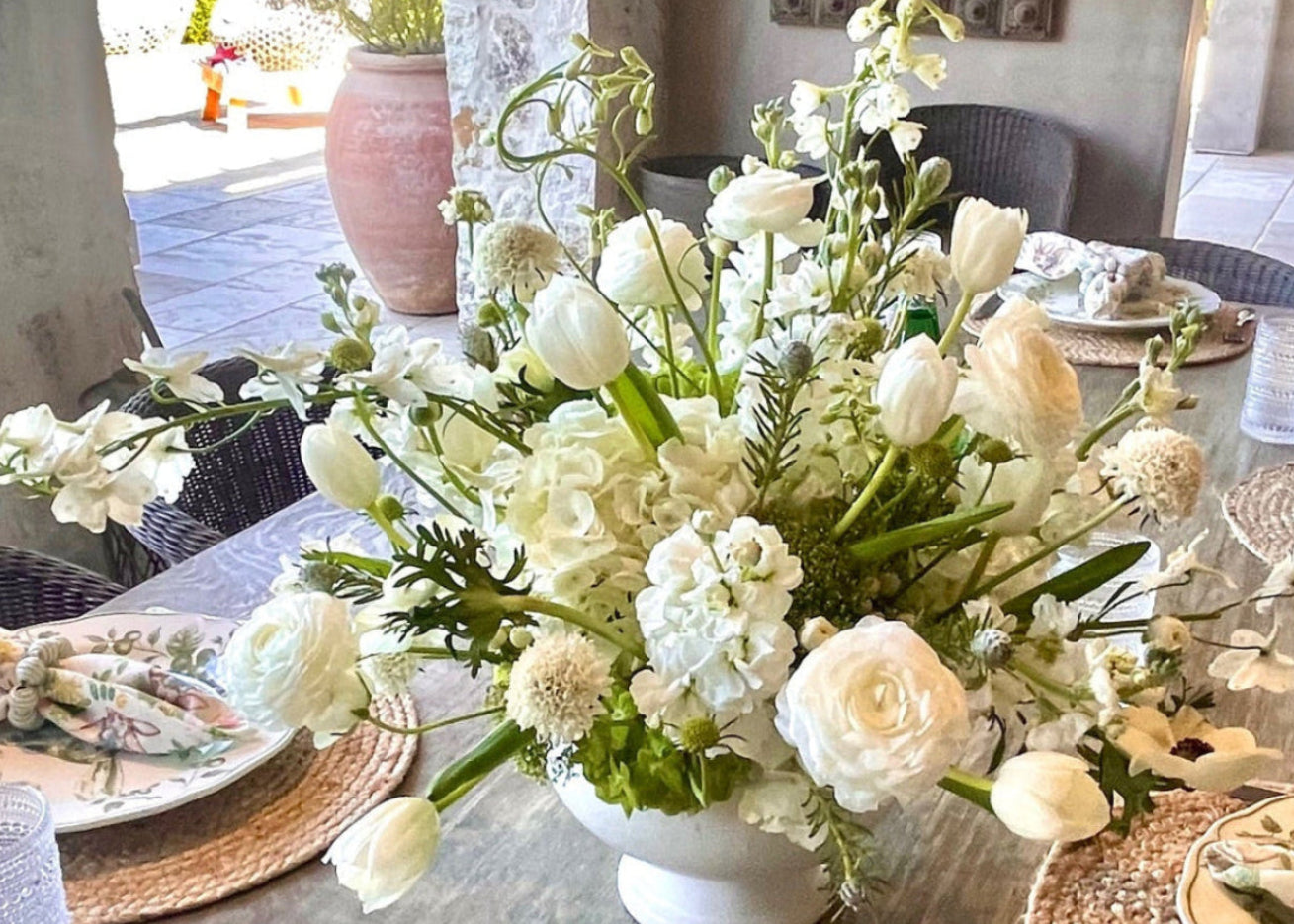 Decorative white floral arrangement on a rustic table with in an outdoor setting.